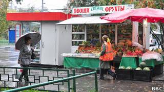 Палатка с овощами и фруктами, мимо которой идут две женщины