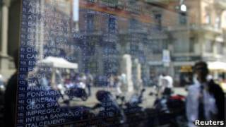 Pedestres passam em frente a tela com cotações de ações da Bolsa de Milão