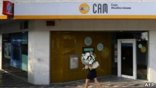 Mulher caminha diante do banco Caja Mediterráneo em Madrid.