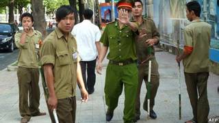 Một cảnh sát giơ tay ngăn phóng viên nước ngoài chụp ảnh tại phiên tòa nhân quyền ở thành phố Hồ Chí Minh hồi tháng Tám với các dân phòng đứng xung quanh