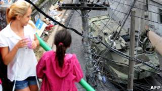 Moradoras observam blindado em rua da Rocinha diante de cabos de ligações clandestinas