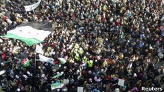 Ujumbe wa nchi za Kiarabu, waliovaa makoti ya njano, wamezungukwa na waandamanaji nchini Syria
