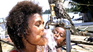 Una mujer y un niño beben agua de una canilla comunitaria