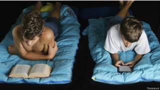 Un joven leyendo un libro y un joven leyendo un libro electrónico, antes de dormir