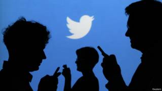 Personas usando su celular con pájaro de Twitter en el fondo.