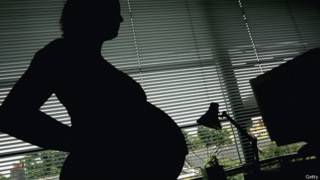 Una mujer embarazada delante de una ventana.