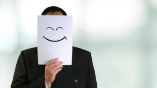 Una persona tapándose la cara con el dibujo de un rostro sonriente