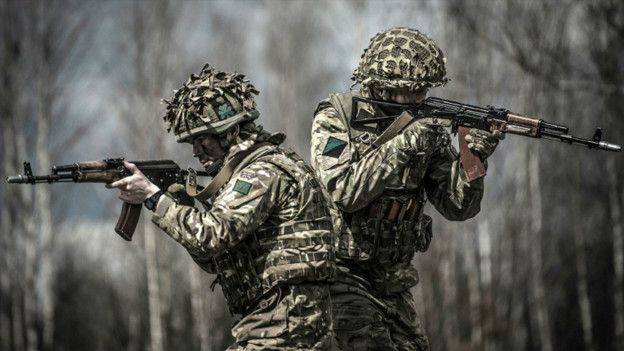 Dos soldados con uniforme de camuflaje, espalda con espalada, sosteniendo sus armas durante un entrenamiento militar ucraniano.