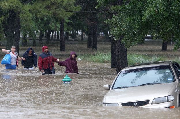 Un grupo de personas camina en la inundación y un carro está hundido