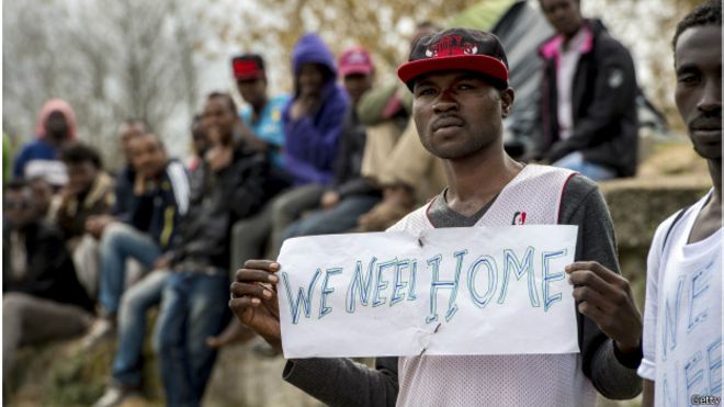 un inmigrante del campamento de refugiados en Calais sostiene una pancarta: "We Need Home" (necesitamos un hogar)