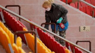 A woman wearing a protective mask and gloves cleans the seating area