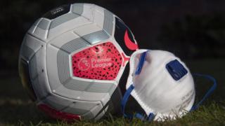 A Premier League branded match ball rests on grass next to a face mask