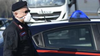 An Italian Carabinieri wearing a respiratory mask stands at a police check-point few kilometers from the small town of Castiglione d'Adda, southeast of Milan