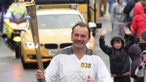 Stephen Martin carries the Olympic Flame in the Torch Relay for the 2012 London Games