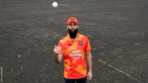 Birmingham Phoenix captain Moeen Ali tosses a ball in the air while wearing his team's shirt and cap