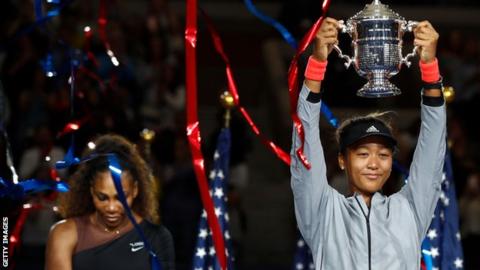 Naomi Osaka lifts US Open trophy as Serena Williams looks at the floor in the background