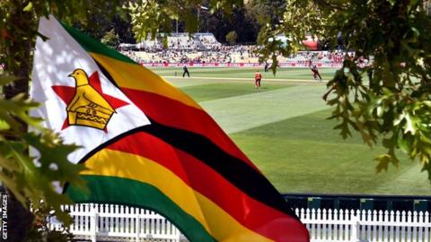 The Zimbabwe flag flies attached to a tree outside a cricket stadium
