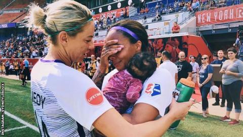 Sydney Leroux celebrates after a game with her baby and a team-mate