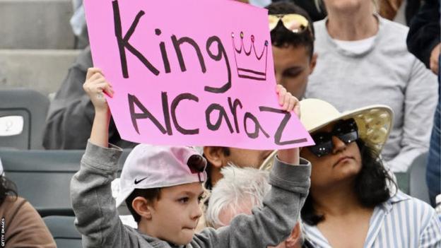 A young instrumentality   holds up   a 'King Alcaraz' motion   during Carlos Alcaraz's lucifer  against Daniil Medvedev successful  the Indian Wells final