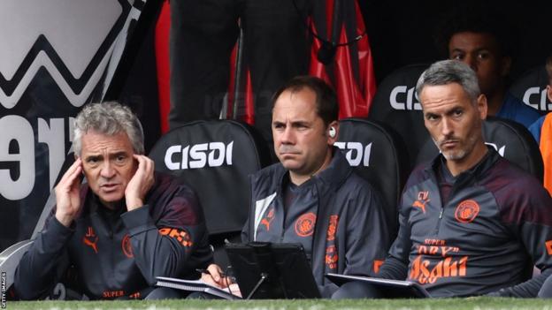 Juanma Lillo using earphones to speak to Pep Guardiola on the Man City bench