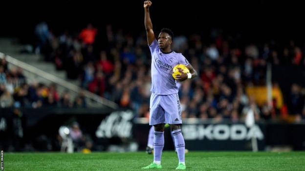 Vinicius Jr holds the ball under his arm and raises his fist in the air to celebrate scoring a goal against Valencia