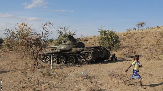 A small child runs past a tank