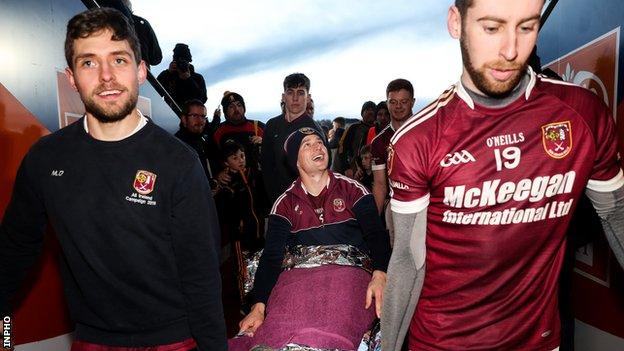 Arron Graffin is taken to the Cushendall dressing-room on a stretcher by team-mates Mark Donaghy and Stephen Walsh after Sunday's Ulster Club Final triumph