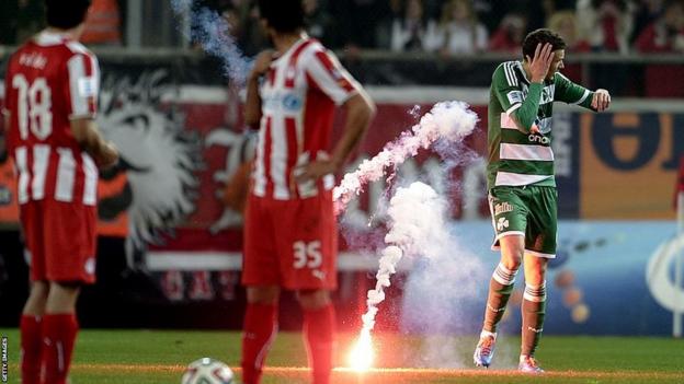 A Panathinaikos player holds his hand to his head after being hit by a flare thrown from the stands.