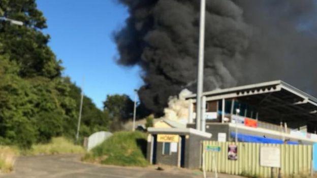 Thick smoke rises from the fire in the changing rooms behind the main stand