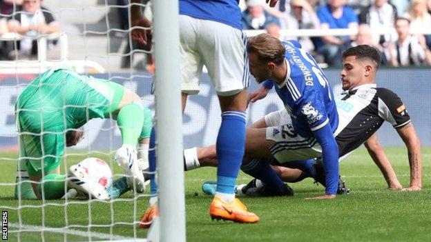 Newcastle's Bruno Guimaraes pokes the ball between the legs of goalkeeper Kasper Schmeichel to score against Leicester