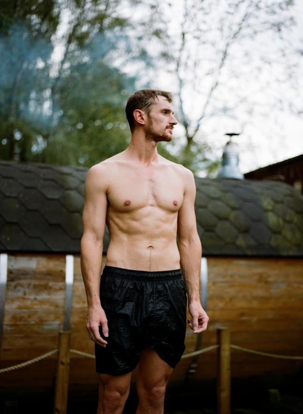 Un homme torse nu portant un short noir se tient devant un sauna