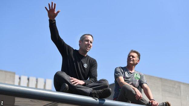 Etienne Stott and Chris Packham make a speech while sitting on top of a bus stop