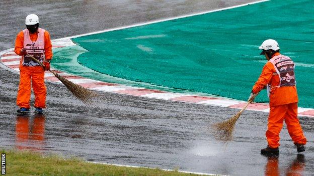 Marshalls attempt to clear puddles on the track with a broom after the race is halted