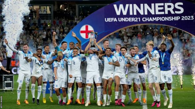 Taylor Harwood-Bellis lifts the European Championships trophy as his team-mates celebrate their victory