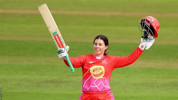 Welsh Fire batter Tammy Beaumont raises her bat and helmet to observe  reaching a century