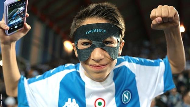 A young Napoli fan wearing a face mask with Osimhen written on it
