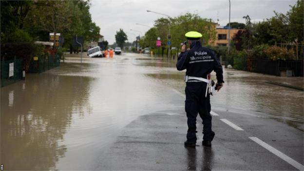 Un agente della polizia municipale osserva da remoto i soccorritori mentre ispezionano un camion su una strada allagata a Castel Bolognese, vicino a Ravenna.