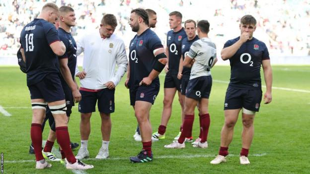 Theo Dan of England looks dejected adjacent  to his England teammates