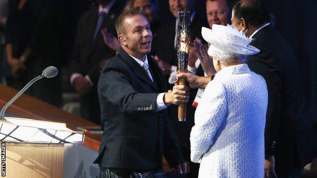 Sir Chris Hoy presents Commonwealth Games Federation president Prince Imran the baton as the Queen looks on