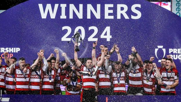 Gloucester players celebrate with their trophy in front of the winners' podium