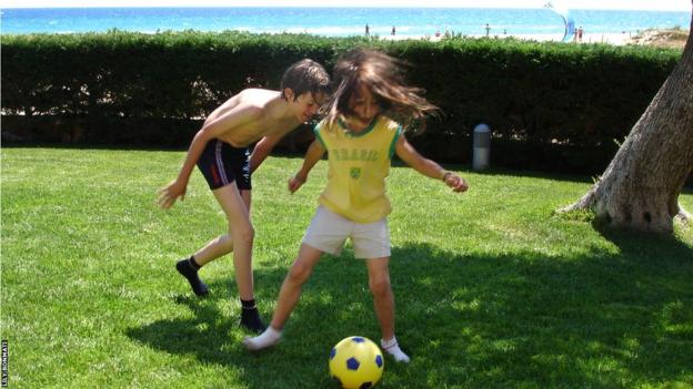 Aitana Bonmati controls the ball ahead of an older male cousin on a strip of grass by a beach