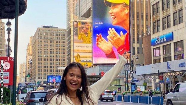 Emma Raducanu smiles and points at a billboard with her face on