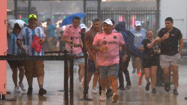 Inter Miami fans get caught in a heavy downpour on their way to see Lionel Messi