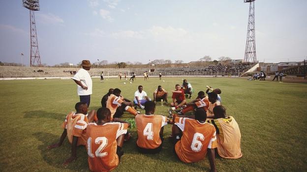 Coach Ian Porterfield gives instructions to seated Zambia players inside a stadium