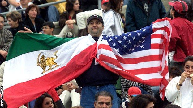 A man holds up the flags of Iran (the flag in use up to the revolution of 1979) and the United States at the 2000 friendly match between the nations
