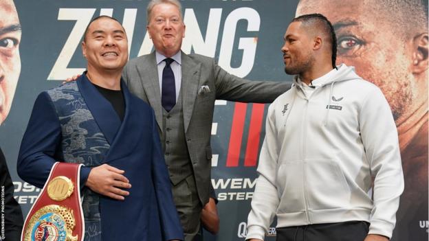 Zhilei Zhang smiles as Joe Joyce looks at him, with promoter Frank Warren standing on a chair in the middle