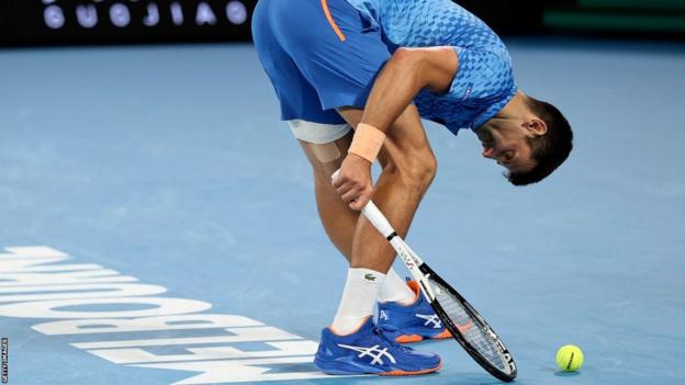 Novak Djokovic stretches out his left hamstring