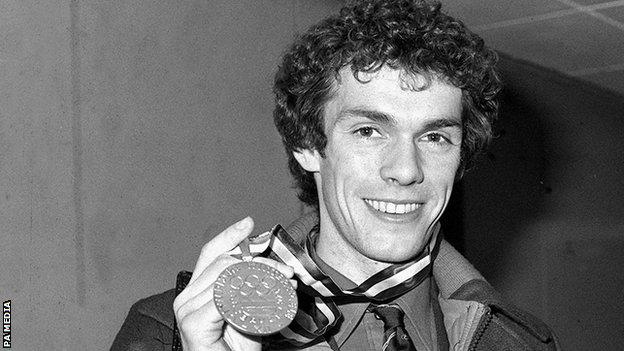 Figure skater John Curry smiles as he holds up his 1976 Winter Olympic gold medal