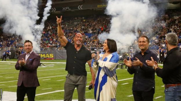 Dwayne Johnson on the field with XFL co-owners Dany Garcia and Gerry Cardinale