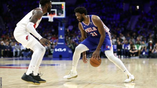Joel Embiid dribbles in front of Deandre Ayton